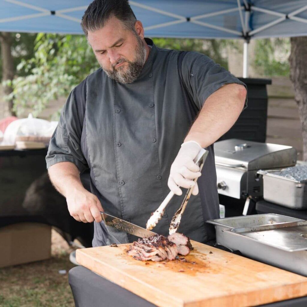 Chef Erik cutting beef at an outdoor Root to Table event.